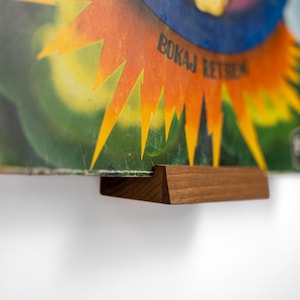 May include: A wooden record holder displaying a vintage album cover. The album art features a burst of orange and yellow rays against a green and blue background. The text "BOKAJ RETIEN" is visible on the cover.