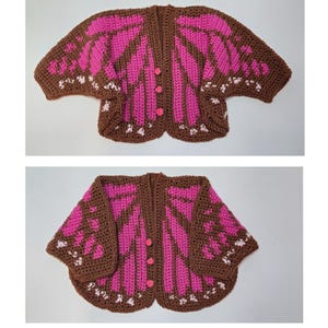 May include: A crochet cardigan featuring a butterfly wing pattern in brown, bright pink, and white. The garment has short sleeves, a rounded hem, and three small pink buttons down the center front. The design mimics the appearance of insect wings.