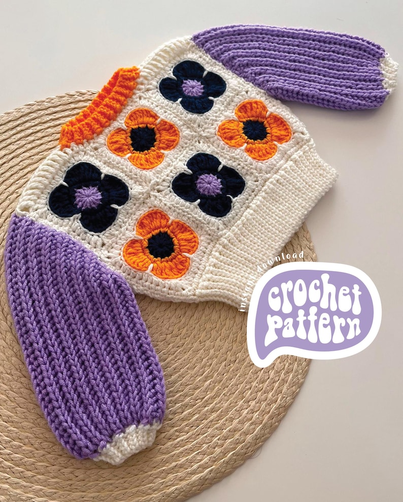 May include: A crocheted baby sweater with a white base and colorful flower motifs. The sleeves are a solid purple color. The sweater is laid on a woven straw mat. The text "crochet pattern" is written in a purple speech bubble.