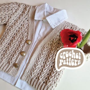 May include: A beige crocheted cardigan with a cable knit pattern and gold buttons. The cardigan is laid out on a white surface with a white shirt underneath. The text "crochet pattern" is written in a brown circle on the image.