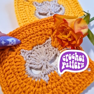 Può includere: Due quadrati all'uncinetto arancioni e gialli, con un motivo a volpe beige chiaro al centro. Una rosa arancione e un adesivo viola con la scritta "crochet pattern" sono visibili. Perfetto per progetti fai-da-te.