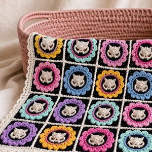 Peut inclure: Une couverture au crochet faite &agrave; la main avec un motif de visage de chat. Chaque carr&eacute; noir est orn&eacute; d'un visage de chat cr&egrave;me entour&eacute; d'anneaux roses, bleus, jaunes et violets. La couverture est bord&eacute;e d'une bordure cr&egrave;me.