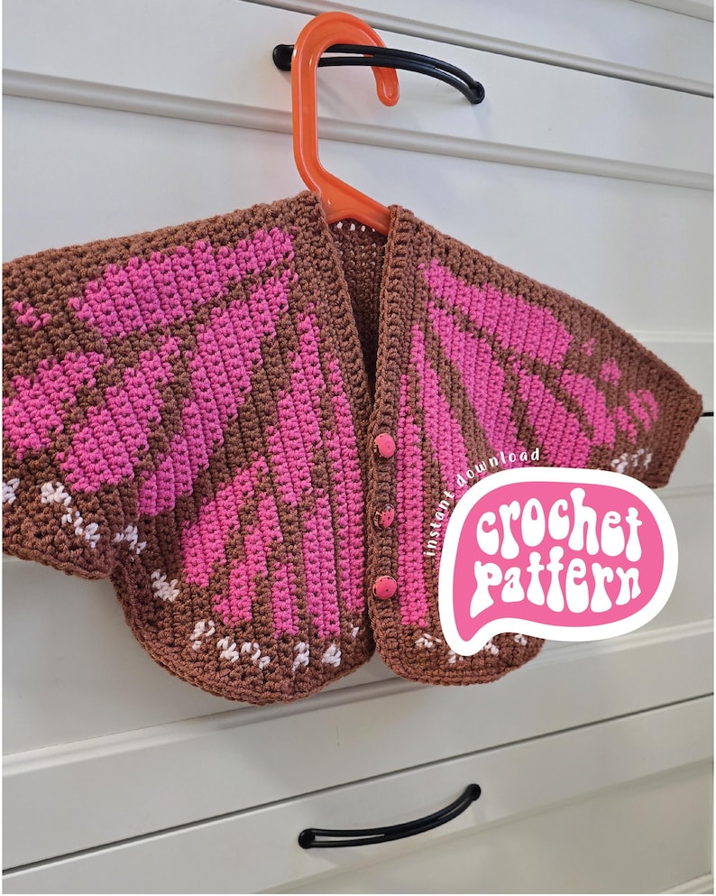 May include: A brown and pink crocheted cardigan featuring a butterfly wing pattern, short sleeves, and three pink buttons down the front. A white speech bubble graphic with the text instant download crochet pattern is overlaid on the garment.