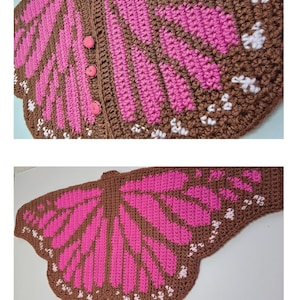 May include: A crochet shawl shaped like butterfly wings in brown, bright pink, and white. The garment features a scalloped edge, a central wing pattern, and three round pink buttons along the front edge to secure the piece when worn.