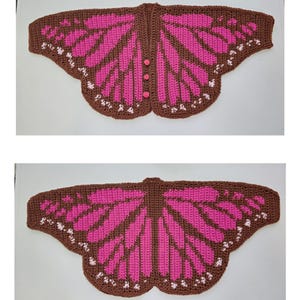 May include: A crochet butterfly wing shawl featuring a brown base with vibrant pink panels and small white accents along the edges. The top view shows three small pink buttons along the center seam, while the bottom view displays the full wing design.
