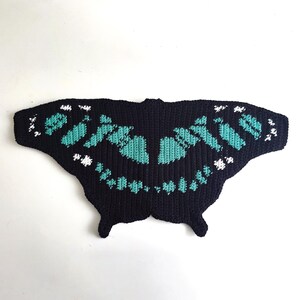 May include: A black, butterfly-shaped crochet piece with turquoise and white accents. The wings feature a detailed pattern, and the overall design is symmetrical. The piece is likely handmade and suitable for decorative purposes.
