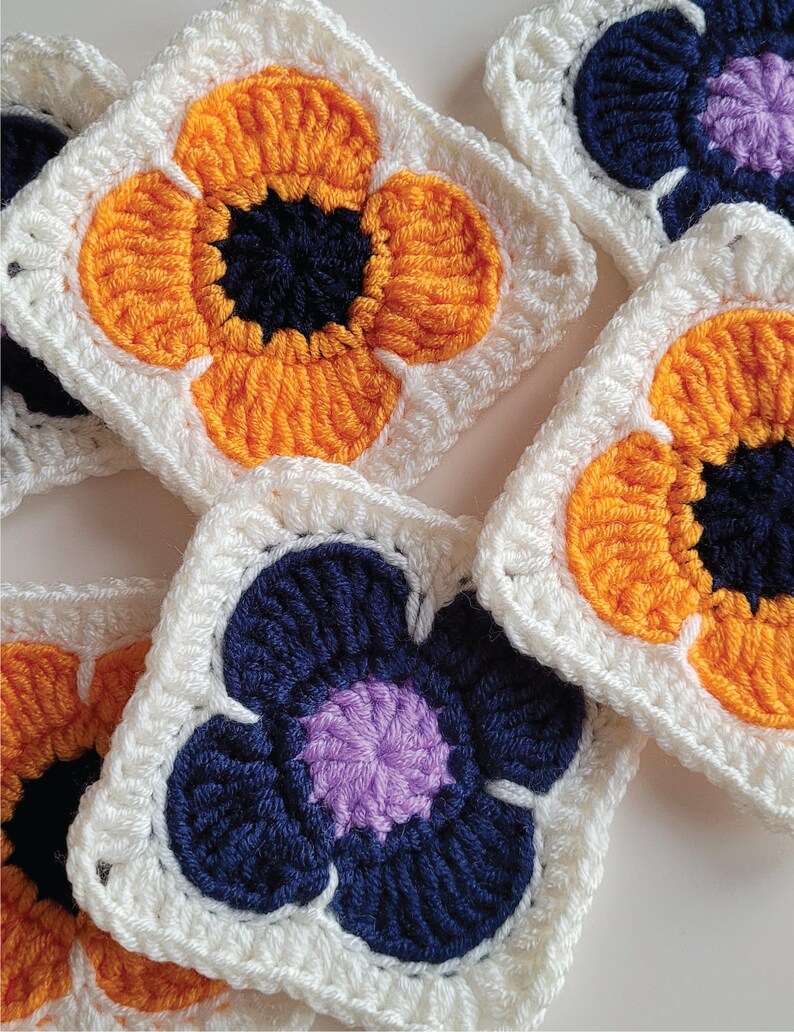 May include: Crocheted flower squares in white, orange, purple, and blue. The squares are made with a granny stitch pattern and feature a flower design in the center.