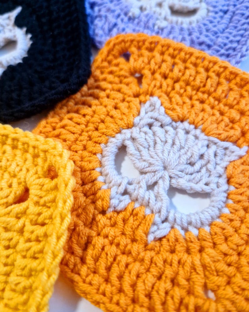 May include: Close-up of several crocheted squares in various colors, including orange, yellow, black, and purple. Each square features a white owl design in the center. The handmade squares are likely part of a larger craft project.