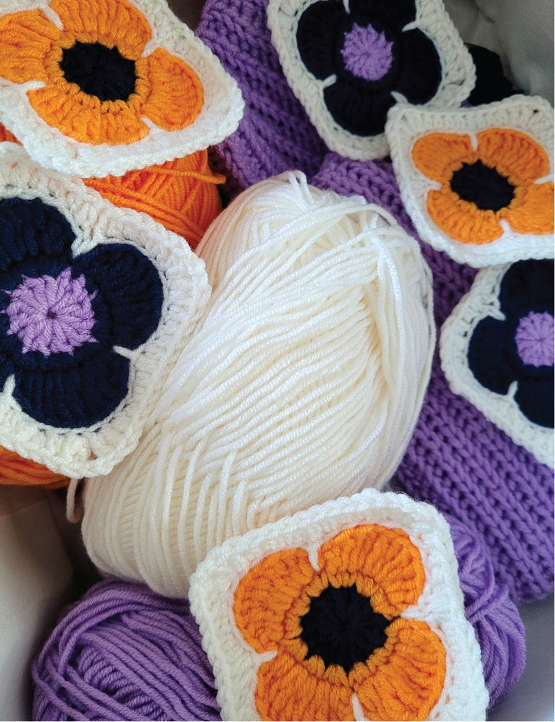 May include: A close-up of a collection of crocheted flower motifs in shades of orange, purple, and white. The flowers are arranged around balls of yarn in purple and white.