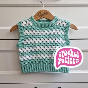 Op de afbeelding: Een mintgroen en wit gehaakt vest, gepresenteerd op een houten hanger. Het vest heeft een granny square patroon met een geribbelde halslijn en zoom. Een roze tekstballon met "crochet pattern" is zichtbaar.