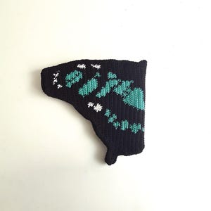 May include: A black, crocheted butterfly wing with turquoise and white accents. The wing features a detailed pattern of turquoise shapes and white dots, creating a textured design. The wing is set against a plain white background.