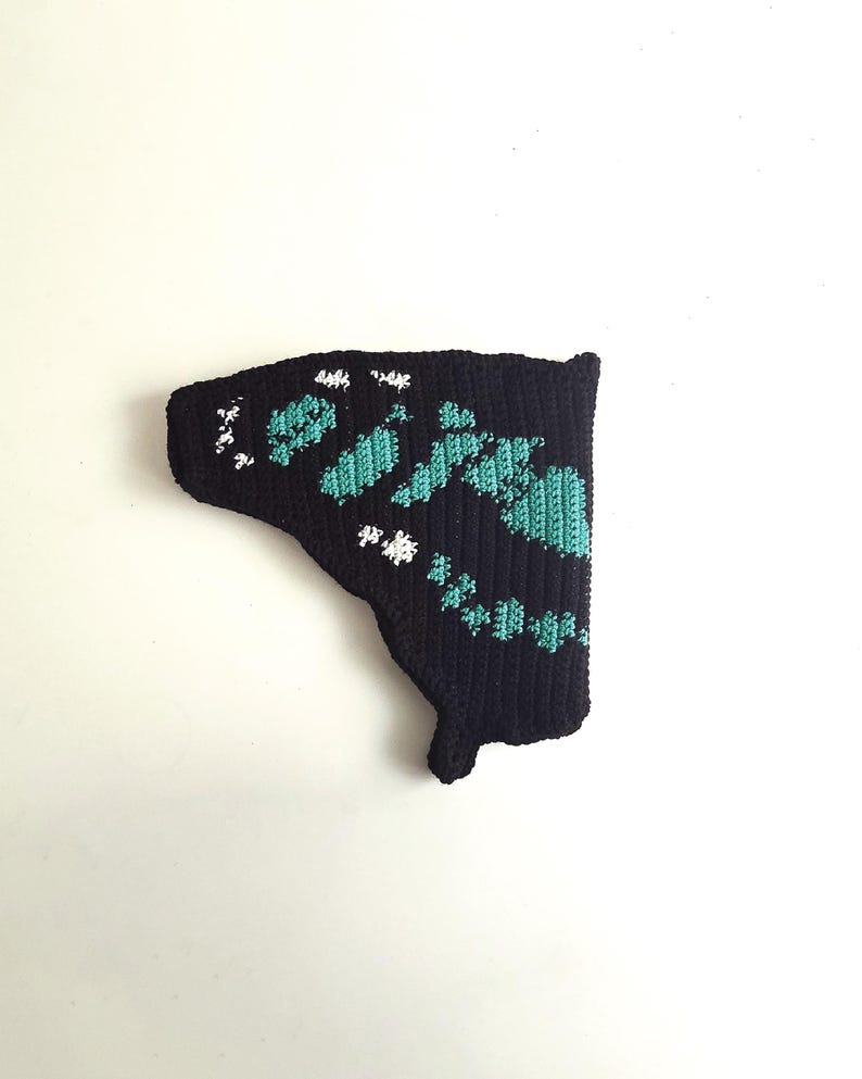 May include: A black, crocheted butterfly wing with turquoise and white accents. The wing features a detailed pattern of turquoise shapes and white dots, creating a textured design. The wing is set against a plain white background.