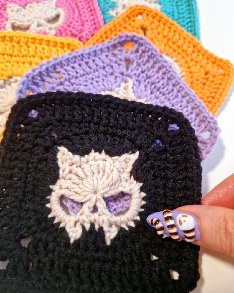 May include: A stack of colorful crochet squares, each featuring a skull design. The squares are in various colors, including black, purple, orange, and pink. The skull is a contrasting color, adding detail to the handmade craft.