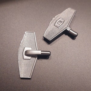 May include: Two silver cufflinks shaped like small aeroplanes. The cufflinks have a textured surface and a small hinge on the side.