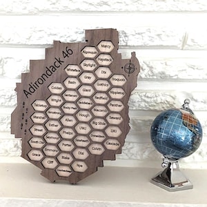 May include: A wooden Adirondack 46 peak map with a globe. The map is shaped like the Adirondack region and lists the names of the peaks. The globe is blue and sits on a silver stand. The map is made of dark wood.