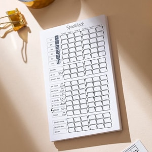 Könnte beinhalten: Ein weißes Blatt Papier mit einem schwarz-weißen Raster und dem Text "Spielblock" oben. Das Raster ist in sechs Spalten unterteilt, die mit "Spiel 1" bis "Spiel 6" beschriftet sind. Das Blatt enthält auch einen Abschnitt mit Würfeln und einer Liste von Punkteoptionen für ein Spiel.