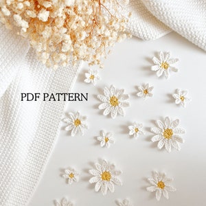 Op de afbeelding: Een witte achtergrond met een verzameling gehaakte witte madeliefjes met gele centra. De tekst "PDF PATTERN" staat in de linkerbovenhoek van de afbeelding.