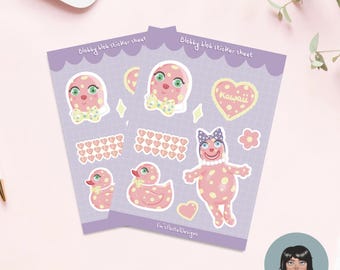 May include: Two sticker sheets with a purple border featuring pink blob characters with polka dots, bows, and hearts. The text "Blobby blob sticker sheet" is at the top. The word "Kawaii" is on a heart-shaped sticker. The artist's name is at the bottom.