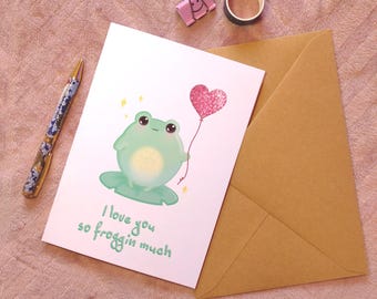 May include: A greeting card with a green frog holding a pink heart-shaped balloon. The card reads "I love you so froggin much".