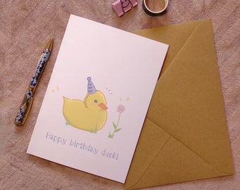 May include: A white card with a yellow duck wearing a blue party hat and a pink flower. The card says "Happy birthday duck!"
