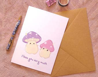 May include: A white card with a pink and purple mushroom illustration and the text "I love you very mush". The card is accompanied by a brown envelope.