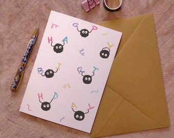 May include: A white card with a happy birthday message written in colorful letters.  The letters are held by black and white cartoon characters with big eyes. The card is in a brown envelope.