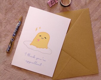 May include: A white card with a cartoon illustration of a yellow egg with a pink heart. The text on the card reads "I think you're eggcellent."