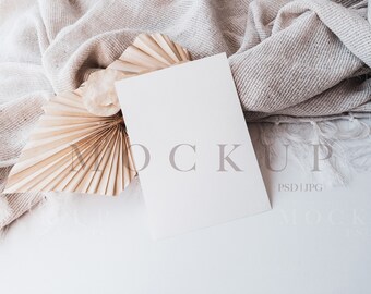 Puede incluir: Una maqueta de tarjeta blanca con una manta tejida beige y un abanico de papel beige. La tarjeta está en blanco y lista para su diseño.