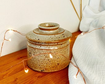Può includere: Un barattolo di ceramica marrone e bianco macchiato con un coperchio. Il barattolo ha una forma arrotondata e un bordo leggermente rialzato. Il barattolo è su una superficie di legno.