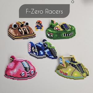 May include: A collection of five pixel art characters from the video game F-Zero Racers. The characters are made of colorful beads and include a pink, green, blue, and brown character. The characters are arranged on a white surface.