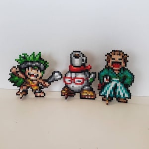 May include: Three pixel art figures made of colorful beads. The figure on the left is green and brown, the middle figure is white, red, and black, and the figure on the right is green, white, and blue.
