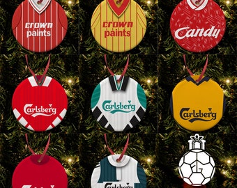Può includere: Nove ornamenti natalizi rotondi con maglie da calcio vintage con loghi di squadra e sponsor. Gli ornamenti sono rossi, gialli, bianchi, verdi e blu. Il testo sugli ornamenti include "Crown Paints", "Candy" e "Carlsberg". L'ornamento inferiore presenta un pallone da calcio bianco con un nastro rosso e il testo "Football Gifts".