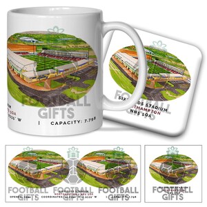 May include: A white mug and coaster set with a football stadium illustration. The mug and coaster feature the text "FOOTBALL GIFTS" and stadium details. The stadium illustration shows green fields, stands, and surrounding landscape. The capacity is 7,798.