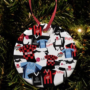 May include: A round white Christmas bauble featuring a pattern of colourful football shirts. The shirts display various logos, including Pizza Hut, GMB, LG, Dabs.com, FXPro, and Pipex.