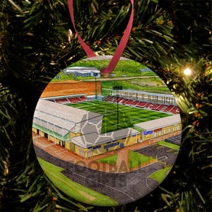 May include: Circular Christmas bauble with a detailed illustration of a football stadium. The bauble has a red ribbon for hanging. The stadium features red seating, a green pitch, and the word FOOTBALL is visible.