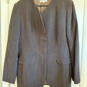 May include: A brown Giorgio Armani blazer with a notched collar and two front pockets. The blazer is made of a striped fabric and is hanging on a black hanger.