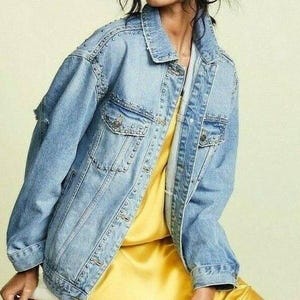 以下が含まれることがあります： シルバーのスタッズがアクセントになった、ライトブルーのデニムジャケット。 ジャケットは、クラシックな襟、ボタン留めのフロント、複数のポケットが特徴です。 黄色のドレスの上に着用されています。