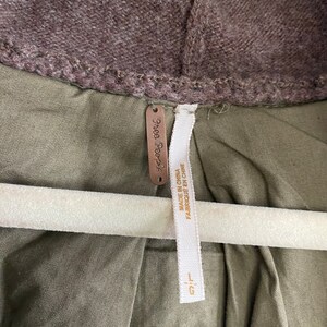May include: Close-up of a jacket with a brown hood and olive green body. The jacket has a tag that says "Free People" and "MADE IN CHINA FABRIQUE EN CHINE". The jacket is hanging on a white hanger.