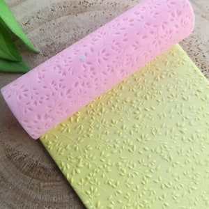 Puede incluir: Dos rodillos de silicona con un patrón de hojas. El rodillo superior es rosa y el rodillo inferior es amarillo.