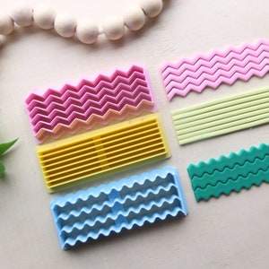 Puede incluir: Conjunto de cinco cortadores de fondant de plástico en rosa, amarillo, azul, verde y verde claro. Los cortadores presentan diferentes patrones, incluyendo zigzags, ondas y líneas rectas.