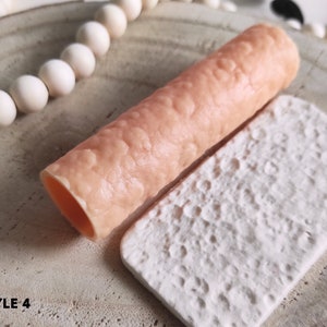 Puede incluir: Primer plano de dos moldes de silicona para hornear. El molde de la izquierda es de color rosa claro y tiene una superficie texturizada. El molde de la derecha es blanco y tiene una superficie texturizada que se asemeja a la superficie de la luna.