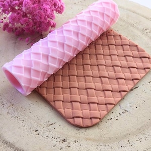 May include: A pink silicone rolling pin with a diamond pattern and a brown silicone mat with a woven pattern. Both are used for decorating cakes and pastries.
