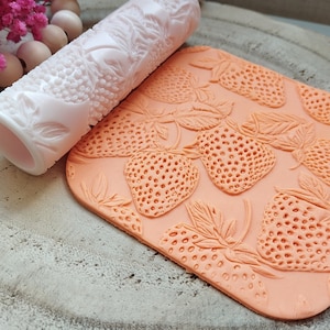 Könnte beinhalten: Ein rosa Nudelholz mit Erdbeer-Design und eine pfirsichfarbene Silikonmatte mit Erdbeer-Design.