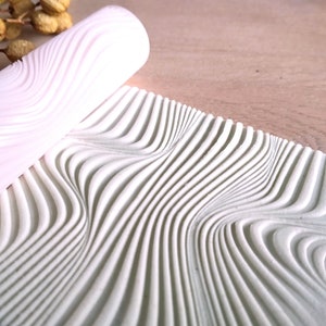 Pode incluir: Um rolo texturizado branco com um padrão ondulado. O rolo é feito de um material macio e flexível e é projetado para criar uma textura única nas superfícies.