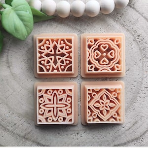 Könnte beinhalten: Vier quadratische, pfirsichfarbene Seifenstücke mit aufwendigen, geprägten Designs. Jedes Stück hat ein anderes geometrisches Muster.