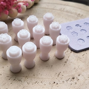 Può includere: Un set di 12 stampini per biscotti in plastica bianca a forma di fiore con diversi design. Gli stampini sono disposti su una superficie di colore marrone chiaro.