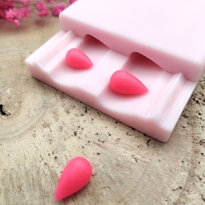 May include: Pink silicone mold with three teardrop-shaped cavities. Three pink teardrop-shaped resin pieces are shown, two in the mold and one removed.