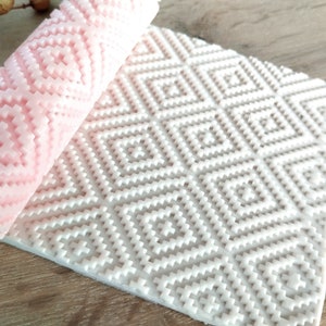 Pode incluir: Um rolo de silicone branco com um padrão geométrico e um rolo de silicone rosa com um padrão semelhante. Ambos são usados para decorar bolos e sobremesas.
