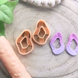 Peut inclure: Deux boucles d'oreilles en résine rose et violette de forme libre avec un trou au centre. Deux emporte-pièces en argile polymère couleur pêche de forme libre similaire avec un trou au centre.
