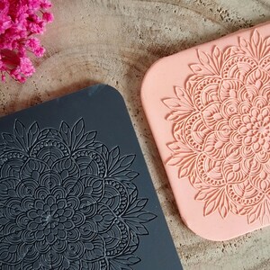 Può includere: Due stampi in silicone per realizzare oggetti decorativi. Uno stampo è nero e l'altro è rosa. Entrambi gli stampi presentano un design di mandala dettagliato.